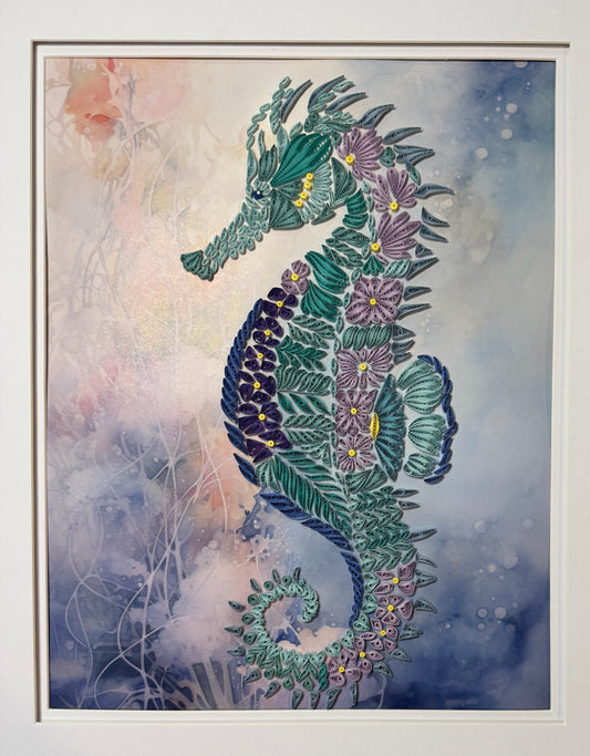 A framed art print featuring a stylized seahorse composed of layered green leaves and purple flowers, set against a soft blue and white watercolor background.