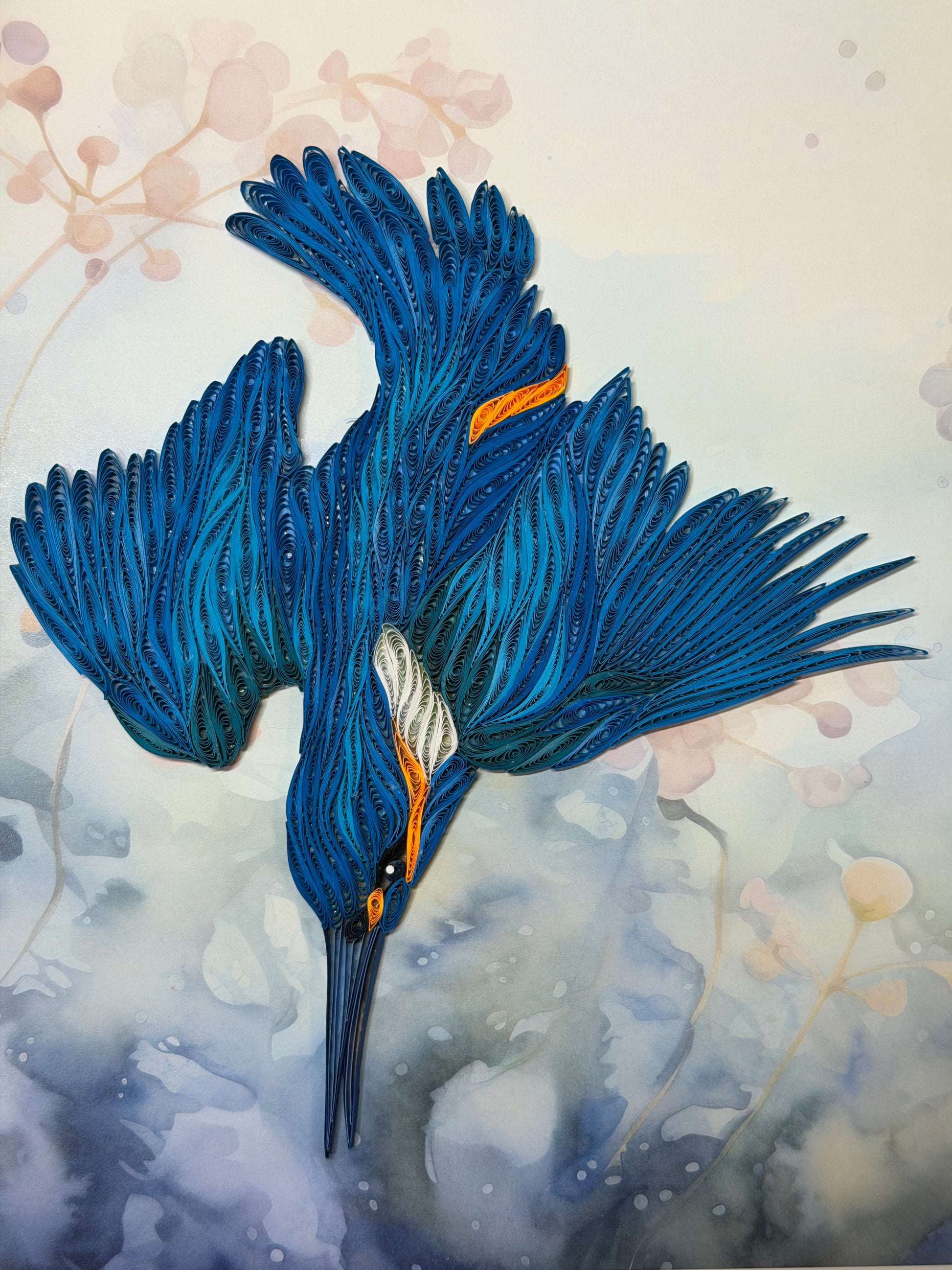 A stylized quilling artwork of a kingfisher with spread wings, rendered in layered blue brushstrokes with small orange and white accents, set against a soft pastel background with faint floral details.